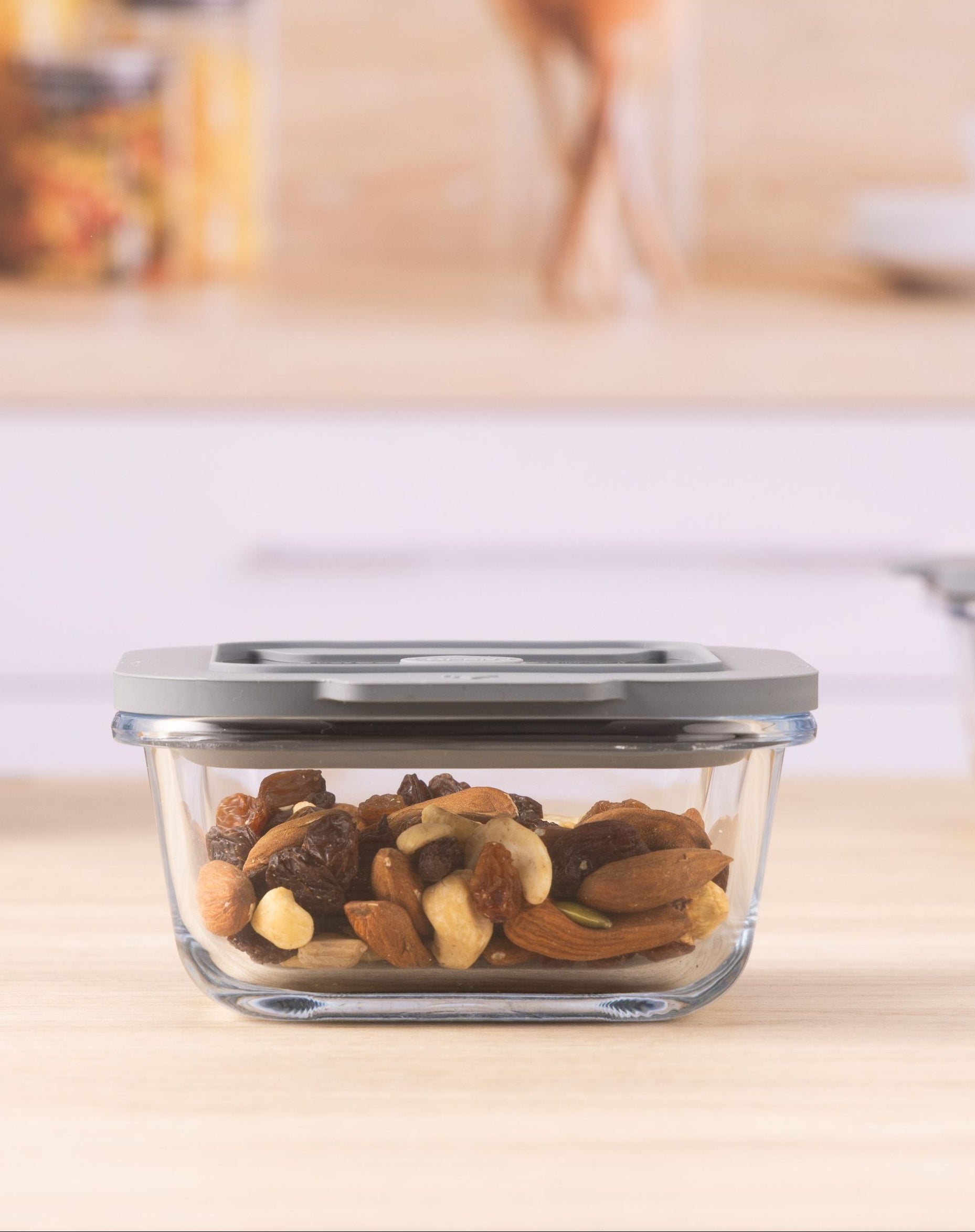 Glass food storage container with lid on a kitchen counter, filled with mixed nuts.