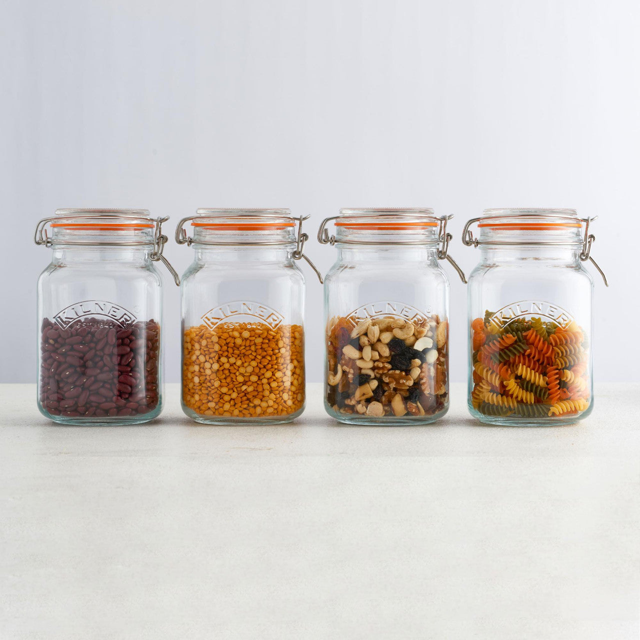 Four glass jars with various dry goods on a white background