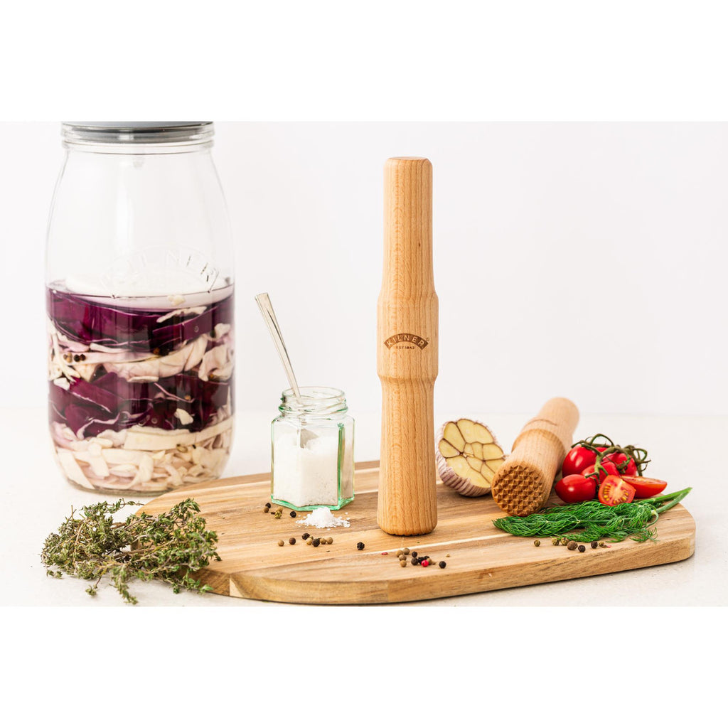 Bamboo kitchen tools including a carafe, mason jar, and rolling pin on a wooden board with vegetables.