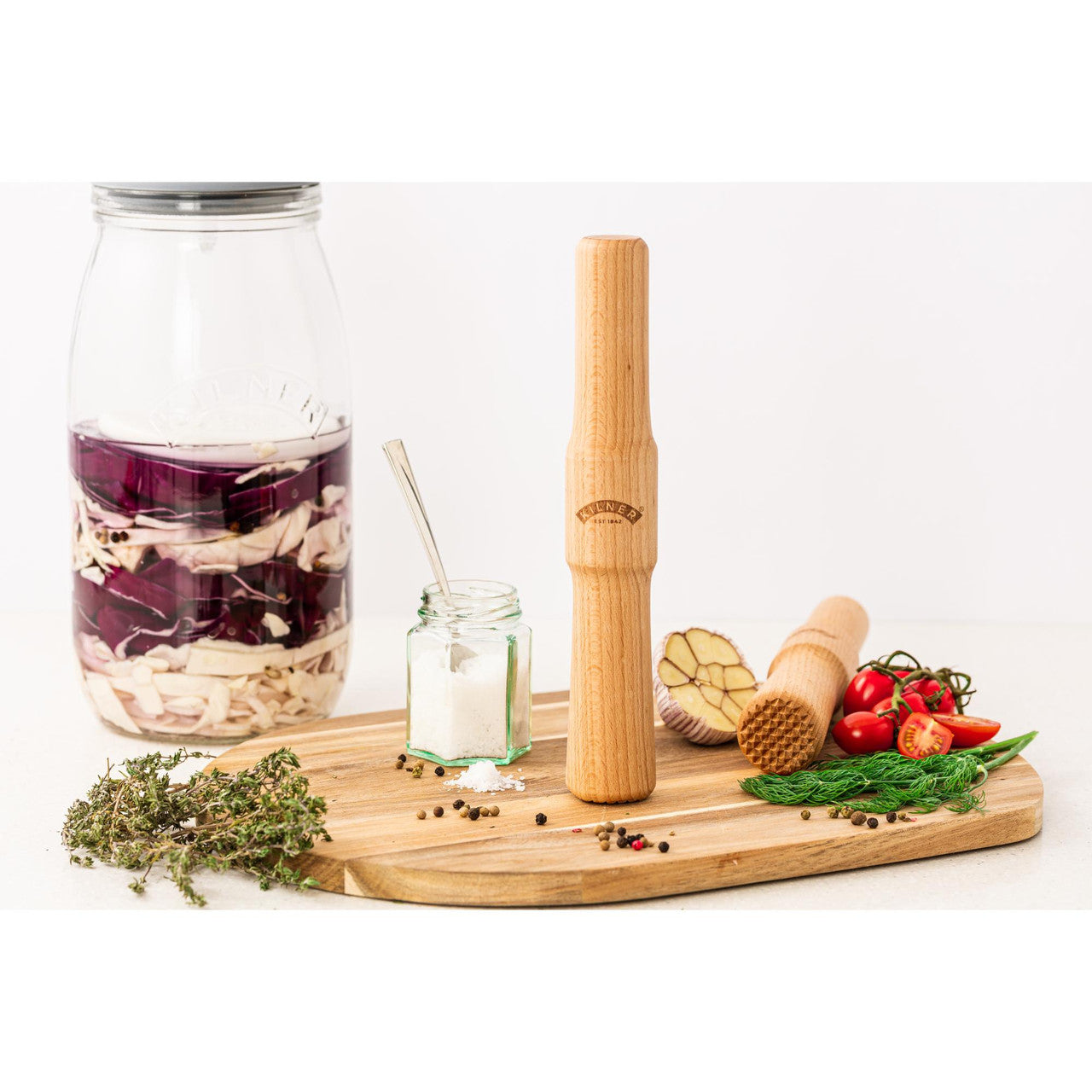 Bamboo kitchen tools including a carafe, mason jar, and rolling pin on a wooden board with vegetables.