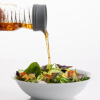 Bowl of salad with a bottle pouring dressing onto it