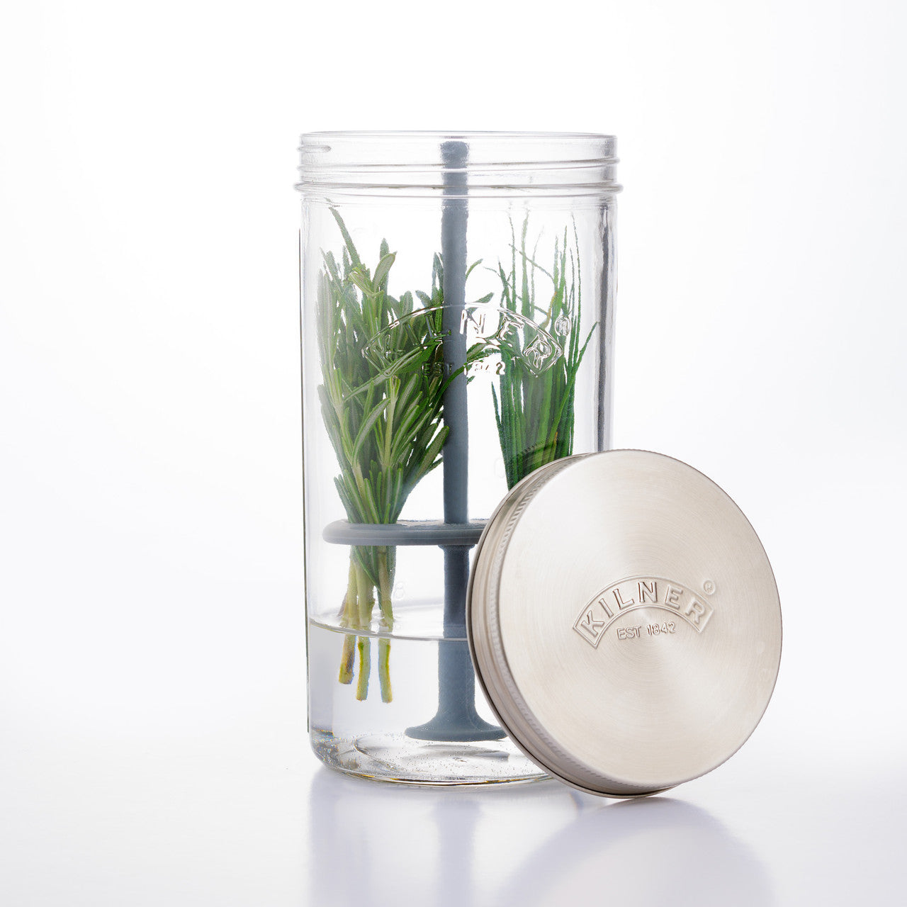 Clear glass container with green herbs and a metal lid on a white background