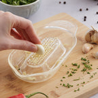 Hand using a garlic press on a wooden cutting board with chopped garlic and herbs.