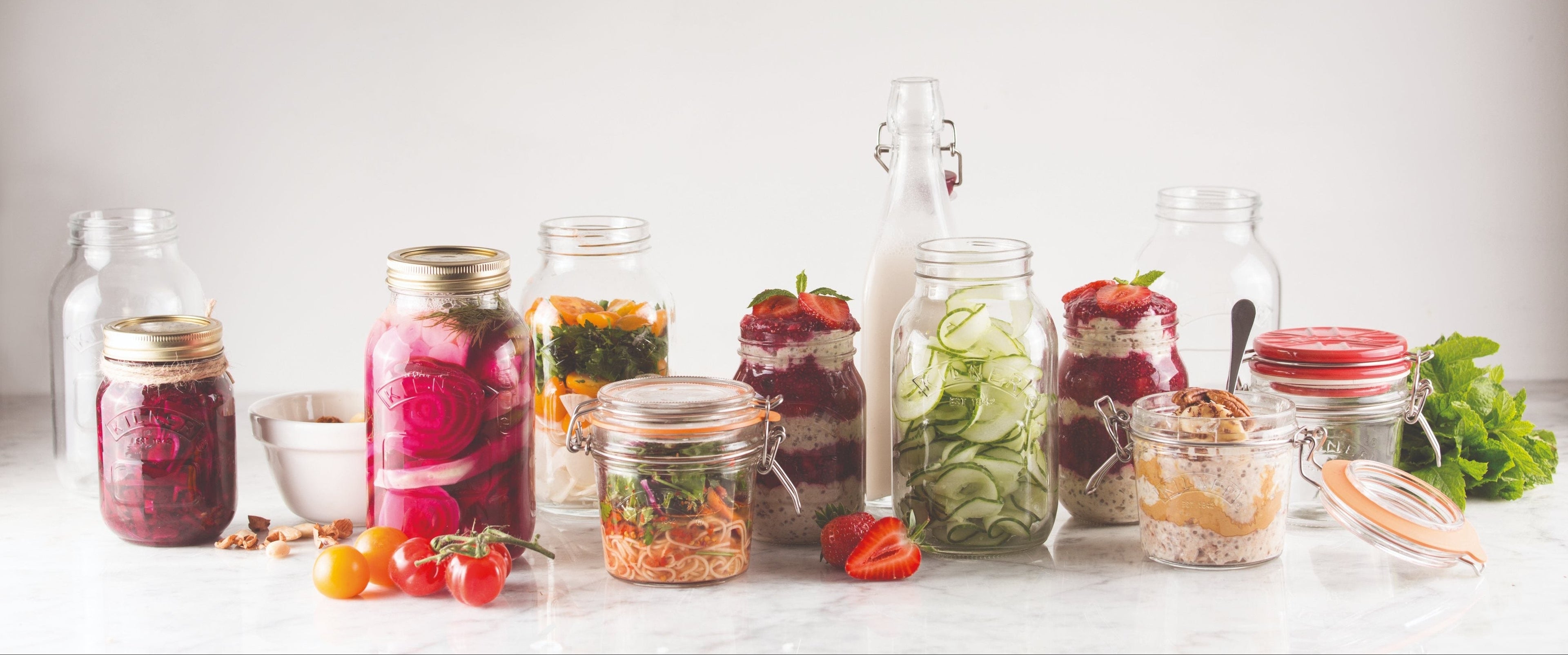 Collection of glass jars with various food items on a white surface